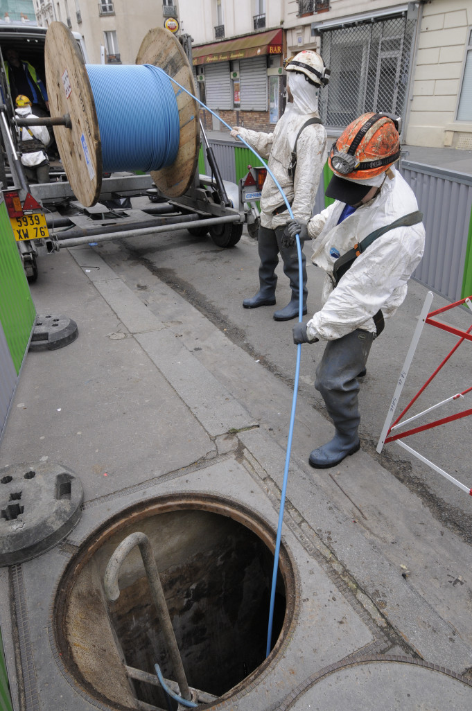 Les techniciens passent un câble de fibre dans les égouts afin de raccorder des immeubles.