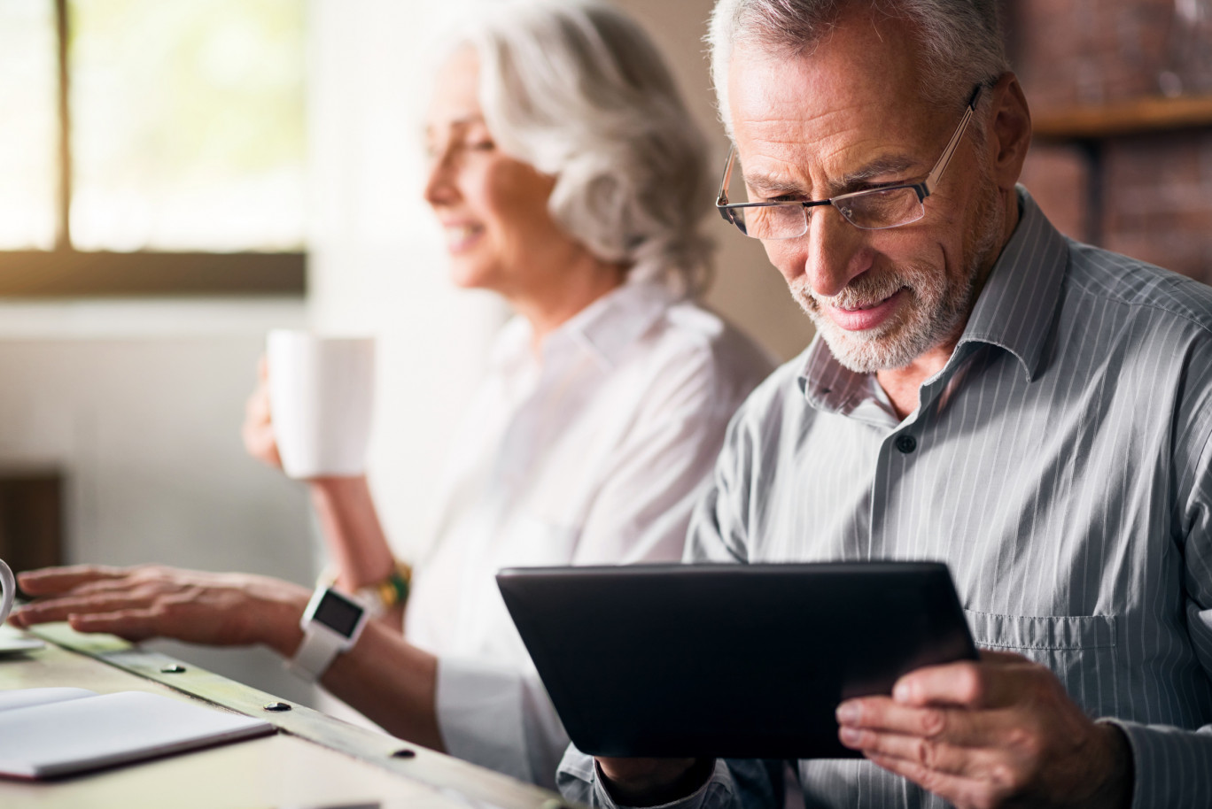 Daily life. Old grey man in glasses using laptop while woman drinking tea and smiling