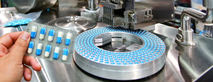 Hand holding blue capsule pack at medicine pill production line, Industrial pharmaceutical concept.banner side